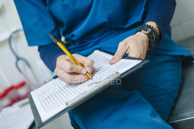 Female nurse writing medical report while sitting in hospital — Stock Photo