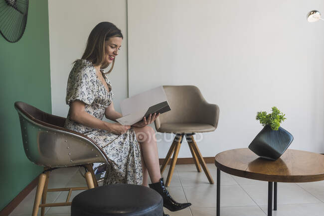 Улыбающаяся деловая женщина читает документ, сидя на стуле — стоковое фото