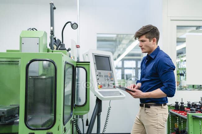 Young male engineer with digital tablet examining machinery equipment in factory - foto de stock