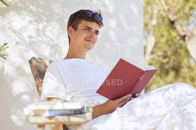 Thoughtful young man looking away while holding book against wall — Stock Photo