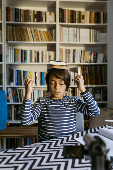 Menino equilibrando livros na cabeça enquanto vlogging câmera de vídeo na sala de estar — Fotografia de Stock