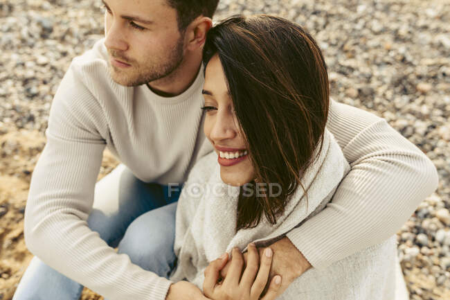 Jeune couple s'embrassant tout en étant assis sur le sable à la plage — Photo de stock