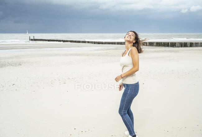 Улыбающаяся женщина, стоящая с закрытыми глазами на пляже — стоковое фото