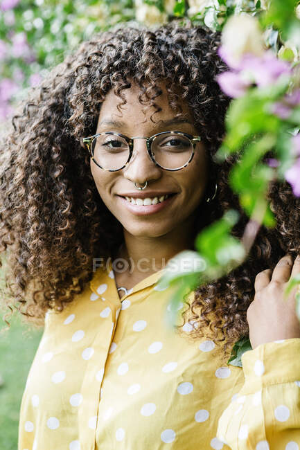Femme aux cheveux bouclés souriant tout en se tenant près du mur vert au parc — Photo de stock