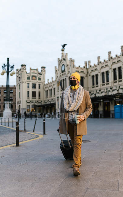 Дивний чоловік у масці на обличчі, тримаючи чашку кави під час прогулянки в місті. — стокове фото
