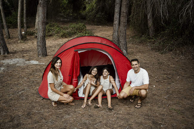 Sonriente familia acampando en el bosque durante las vacaciones - foto de stock