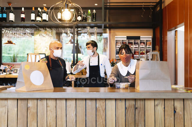 Male and female owner with chef talking while preparing take out food in bar during COVID-19 — Stock Photo