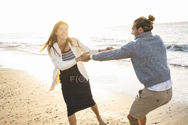 Cheerful young couple holding hands while enjoying at beach during sunny day - foto de stock