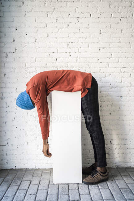 Hombre adulto medio inclinándose sobre el pedestal contra la pared de ladrillo blanco - foto de stock
