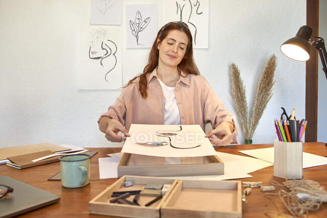Artista donna in possesso di disegno sopra cornice alla scrivania in soggiorno — Foto stock