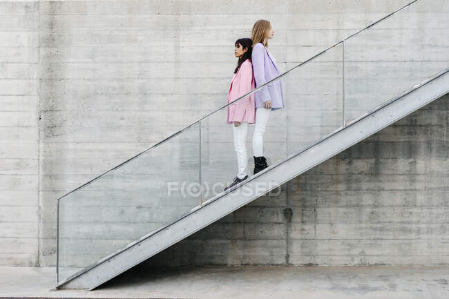 Young siblings back to back standing on steps by wall - foto de stock