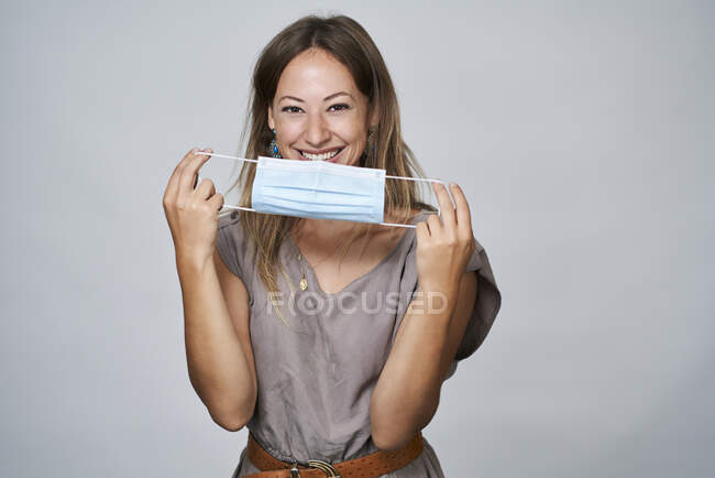 Lächelnde Frau mit schützender Gesichtsmaske während COVID-19 vor grauem Hintergrund — Stockfoto