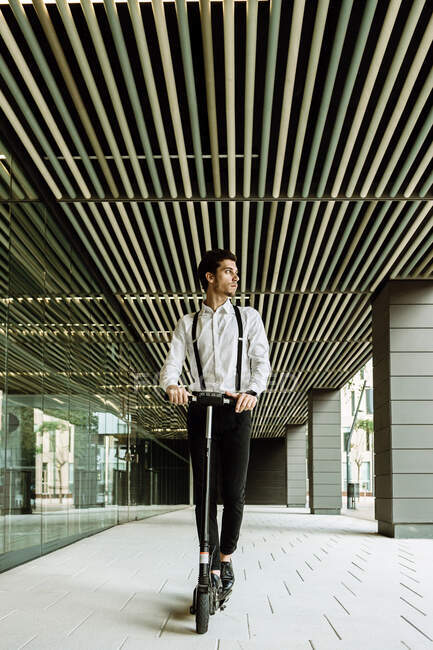 Businessman on electric push scooter near modern glass office building — Stock Photo