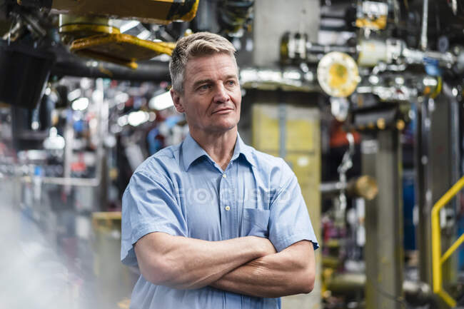 Uomo d'affari maturo con le braccia incrociate guardando altrove mentre in piedi nell'industria — Foto stock
