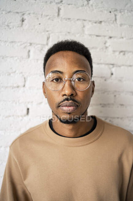 Hombre adulto medio con expresión en blanco usando anteojos contra pared de ladrillo blanco - foto de stock