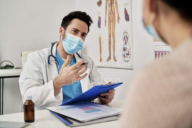 Чоловічий лікар з захисною маскою для обличчя розмовляє з пацієнтом у клініці. — стокове фото