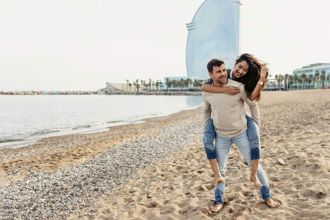 Petit ami donnant piggyback tour à petite amie contre le ciel à la plage — Photo de stock