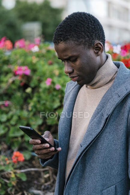 Man wearing jacket using mobile phone while standing at park — Stock Photo