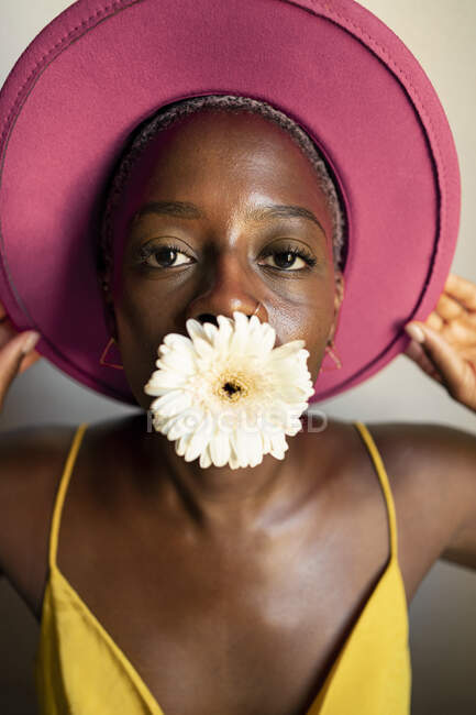 Mulher com flor branca na boca usando chapéu rosa em casa — Fotografia de Stock