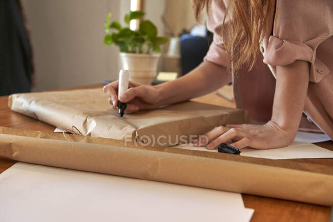 Mensaje de escritura freelancer femenino en paquete envuelto en el escritorio en la sala de estar - foto de stock