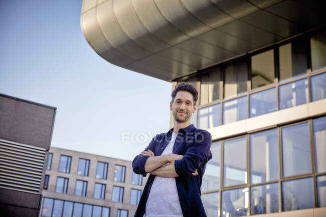 Selbstbewusster Geschäftsmann steht mit verschränkten Armen vor Gebäude — Stockfoto