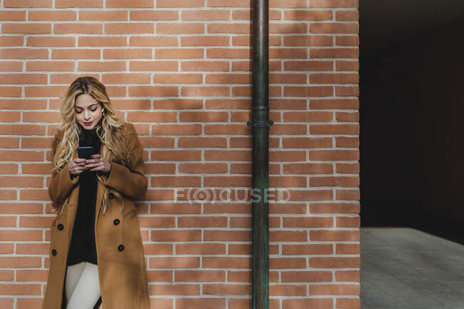 Giovane donna utilizzando smart phone durante l'ascolto di musica contro muro di mattoni — Foto stock