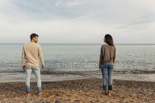 Jovem casal de pé na areia contra o céu na praia — Fotografia de Stock