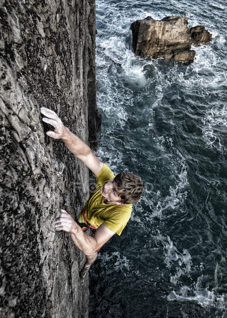 Giovane scalatore di roccia maschio arrampicata scogliera dal mare — Foto stock