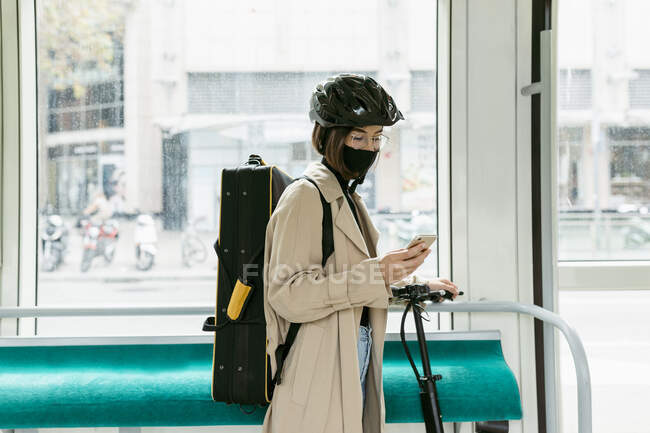 Mujer con bolsa de instrumentos y scooter push usando teléfono móvil mientras está de pie en tranvía — Stock Photo