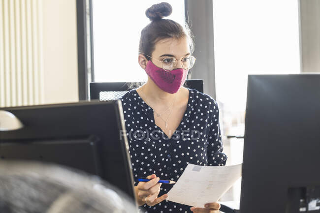 Empresaria con máscara facial trabajando en la computadora mientras está sentada en la oficina - foto de stock