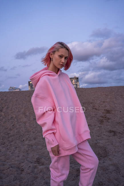 Ritratto di giovane donna con capelli rosa che indossa una camicia rosa con cappuccio sulla spiaggia al tramonto — Foto stock
