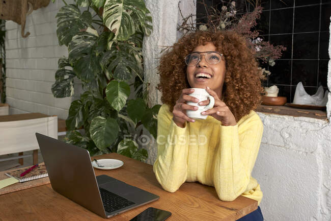 Trabalhador freelance alegre olhando para cima enquanto segurando xícara de café no café — Fotografia de Stock