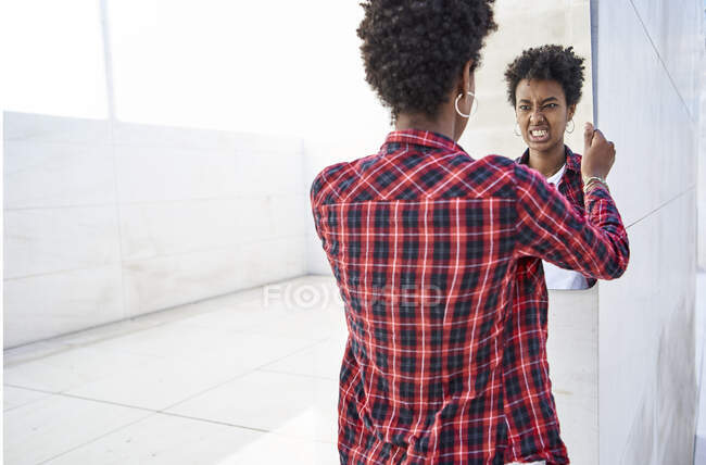 Young female hipster making a face while looking at mirror reflection against wall — Stock Photo