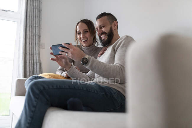 Casal feliz usando telefone inteligente enquanto sentado em casa — Fotografia de Stock