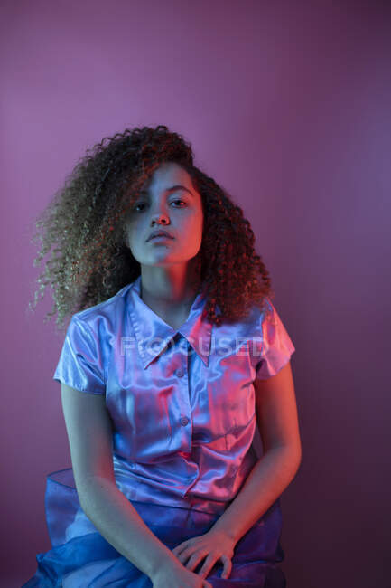 Selbstbewusste junge Frau sitzt vor farbigem Hintergrund im Rotlicht — Stockfoto