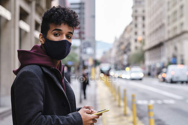 Junger Mann mit Mundschutz und Handy in der Stadt — Stockfoto