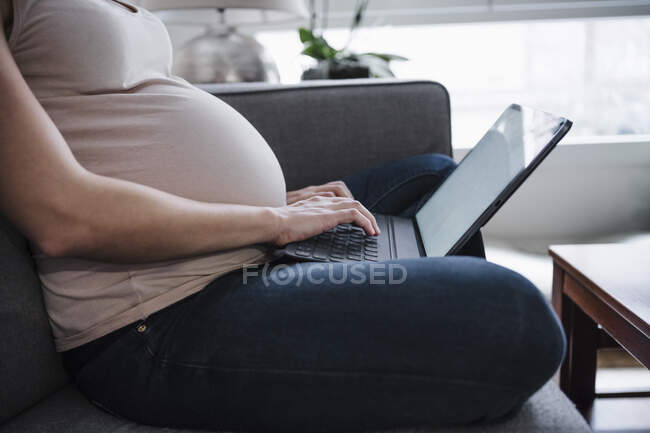 Pregnant woman using laptop while sitting on sofa at home — Stock Photo