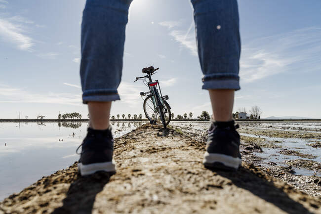 Велосипед, який видно на ногах жінки, що стоїть на стежці в дельті Вебро в сонячний день. — стокове фото
