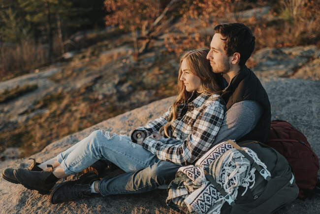 Young couple sitting together on rocky surface during autumn hike — Photo de stock
