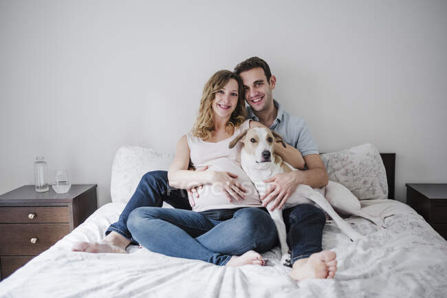Couple souriant avec chien relaxant sur le lit contre le mur à la maison — Photo de stock