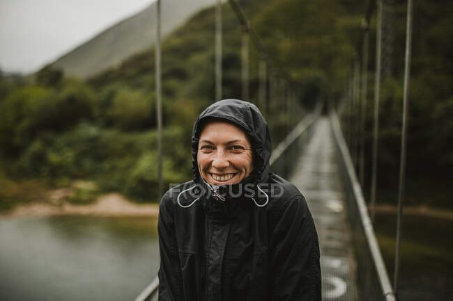 Smiling woman standing on suspension bridge over Sella river on rainy day — Stock Photo