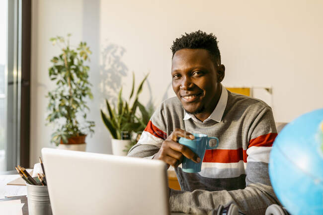 Smiling male entrepreneur sitting with coffee cup in home office —  communication, portrait - Stock Photo | #481863418