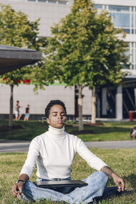Young businesswoman with laptop meditating at park during sunny day — Stock Photo