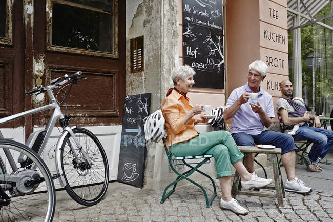 Turistas con bicicleta eléctrica tomando café mientras están sentados en el casco antiguo de Dresde, Alemania - foto de stock