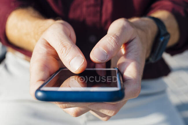 Businessman using smart phone while sitting outdoors - foto de stock