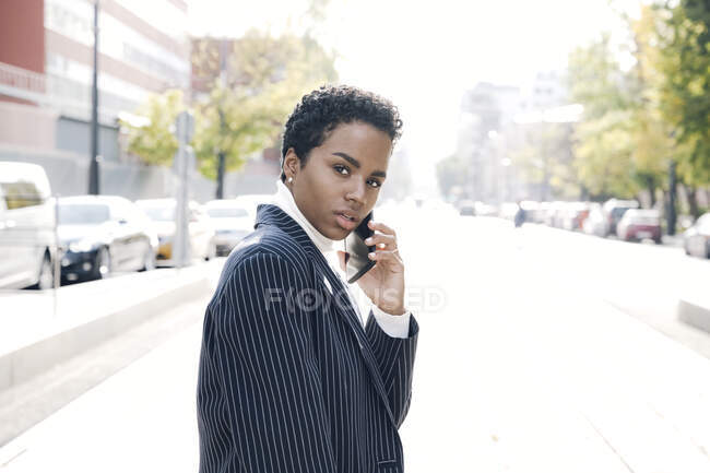 Femme d'affaires confiante parlant par téléphone intelligent dans la rue en ville pendant la journée ensoleillée — Photo de stock