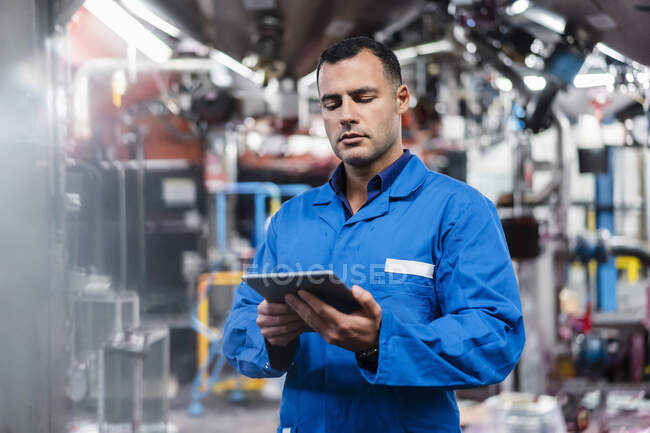 Ingenieur im blauen Mantel arbeitet in Fabrik an digitalem Tablet — Stockfoto
