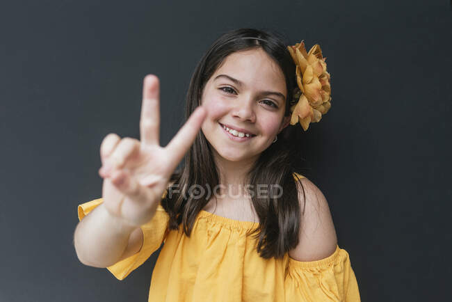 Primer plano de la chica sonriente con diadema amarilla que muestra signo de paz contra fondo negro - foto de stock