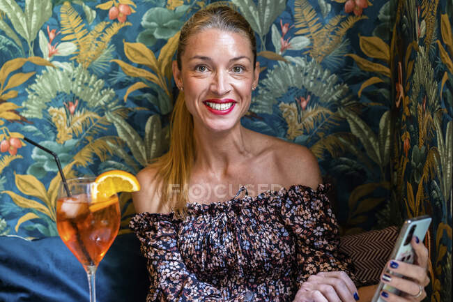 Retrato de mujer adulta sentada en la mesa del restaurante con teléfono inteligente en la mano - foto de stock