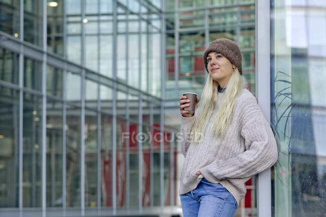 Jeune femme avec café debout contre le bâtiment moderne dans la ville — Photo de stock